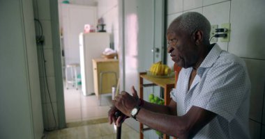 Afro-Amerikalı yaşlı bir adam, bir baston tutan, sakin, bilgelik yayma ve günlük mutfak ortamında iç gözlem