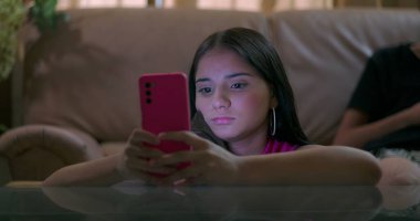 Genç çocuk, akıllı telefonlara odaklandı. Kanepede, pembe akıllı telefona kapılmış genç bir kıza geçti. Sosyal medya bağımlılığını ve gençliğe dijital bağımlılığı gözler önüne serdi.