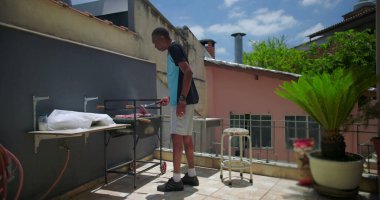 Afrika kökenli Amerikalı bir adam terasta et pişiriyor, güneşli bir açık şehir ortamında barbekü hazırlıyor.