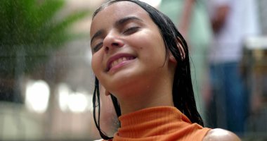 Genç kız ferahlatıcı su spreyi altında, yüzü huzurlu bir ifadeyle rahatlamış, sıcak bir yaz gününde neşeli ve kaygısız bir anı yakalıyor.