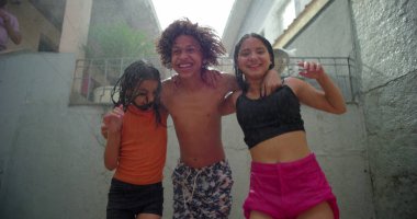 Çocuklar arka bahçedeki toplanma sırasında su altında gülüp kucaklaşıyorlar, neşeli ve kaygısız anları canlı ve oyuncu bir açık hava ortamında paylaşıyorlar