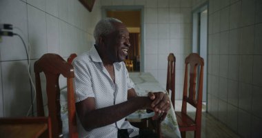 Yaşlı Afro-Amerikalı adam mutfakta oturmuş içten bir şekilde gülüyor ve gülüyordu. Huzurlu ve samimi bir evde mutluluk ve neşe ifade ediyordu.