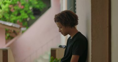 Genç Afrikalı Amerikalı bir çocuk duvara yaslanmış, dalgın ve dalgın görünüyor, hayatı ve duyguları yansıtıyor, umut ve canlı tonları sembolize ediyor.