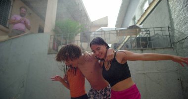 Çocuklar arka bahçedeki toplanma sırasında su altında gülüp kucaklaşıyorlar, neşeli ve kaygısız anları canlı ve oyuncu bir açık hava ortamında paylaşıyorlar