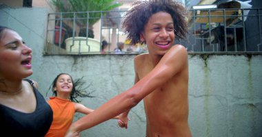 Neşeli gençlik dışarıda oynuyor ve gülüyor, canlı bir toplum atmosferinde el ele tutuşuyor yukarıdan su damlıyor, kaygısız eğlence ve bağlantıyı kutluyor.