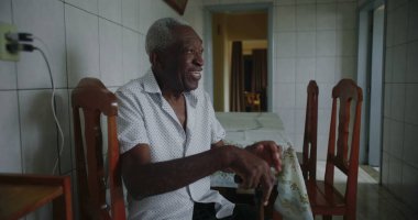 Yaşlı Afro-Amerikalı adam mutfakta oturmuş içten bir şekilde gülüyor ve gülüyordu. Huzurlu ve samimi bir evde mutluluk ve neşe ifade ediyordu.