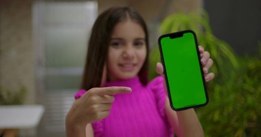 Elinde yeşil ekran krom anahtarı olan akıllı telefonu tutan, neşeli bir ifadeyle boş ekrana bakan, açık bir evde kişiselleştirilebilir içeriği gösteren genç bir kız.