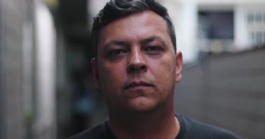 Şehir sokaklarında ciddi bir adamın yakın çekimi, sakin ve nötr yüz ifadesi, modern şehir atmosferi, iç gözlem anı, otantik şehir yaşam tarzı