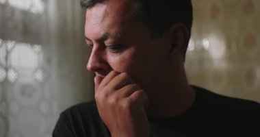 İnsan endişeli ve kederli hissediyor, elleri ensesinde dinleniyor, üzüntü ve pişmanlık ifade ediyor, dantel perdeler ve yansıtıcı bir atmosferde duvarlarla çevrili.