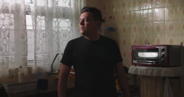 Eski tarz bir mutfakta dikilip pencereye doğru düşünceli bir şekilde bakan klasik fayanslar ve doğal ışıkla nostaljik bir ortam yaratan bir adamın yakın çekimi.