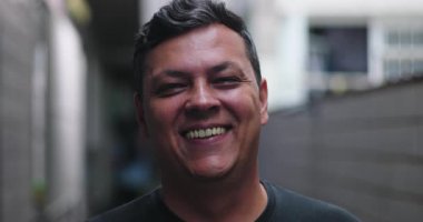 Kentsel sokakta gülümseyen bir adamın yakın çekimi, neşeli ve rahat bir ifade, arkadaş canlısı bir hava, çağdaş şehir atmosferi, dışarıda yakalanan otantik insani duygular.