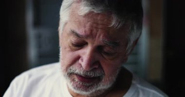 Kafasını nemli gözlerle eğen yaşlı bir adam ve titreyen bir ifade, derin duygusal karışıklığı ve evde yalnızlığın sessiz acısını ortaya koyuyor.