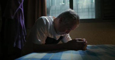 Yaşlı bir adam başını öne eğip yatağa yaslanıyor. Düşüncenin sakin, sakin, düşünceli, sakin atmosferini yansıtıyor.