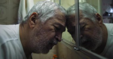 Yaşlı adam ayna karşısında dinleniyor, gözleri kapalı, bitkinliğini ve umutsuzluğunu ifade ediyor sessiz bir iç gözlem ve mücadele anında.