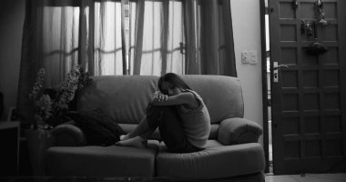 Kanepede oturan genç bir kız, bacakları vücuduna yakın tutulmuş, kafası kollarında dinleniyor, izolasyon, çocukluk bunalımı ve akıl hastalığı belirtileri gösteriyor.