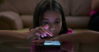 Parlak akıllı telefon ekranına odaklanırken kollarında dinlenen genç kız dijital bağlılık, teknoloji kullanımı ve modern çocukluk alışkanlıklarını gösteriyor