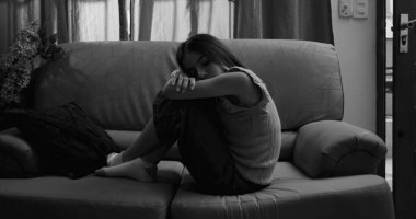 Kanepede oturan genç bir kız, bacakları vücuduna yakın tutulmuş, kafası kollarında dinleniyor, izolasyon, çocukluk bunalımı ve akıl hastalığı belirtileri gösteriyor.