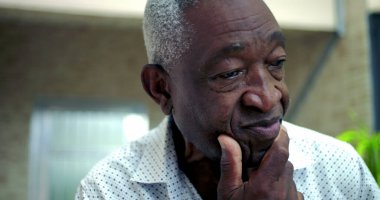 Yaşlı Afro-Amerikan bir adam, elinde dinleniyor, endişe ve pişmanlık gösteriyor, bir iç gözlem anında geçmiş kararları yansıtıyor açık hava ortamında