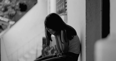 Duvarda tek başına oturan genç bir kız, yüzünü ellerle kapatıyor, umutsuzluk ve üzüntü içinde, çocukluk yalnızlığının ve hassasiyetinin temalarını temsil ediyor.