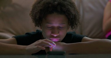 Çocuğun yakın çekimi parlak akıllı telefon ekranı, boş ifade, duygusal kopukluk, yalnızlığı vurgulama ve teknolojinin izole edici etkilerine odaklandı.