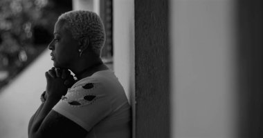 Duvara yaslanmış Afrika kökenli Amerikalı bir kadın, dua ederken ellerini sımsıkı tutuyor, duygusal kargaşa sırasında ilahi rehberlik ve güç arıyor, hayatın zorluklarını yansıtıyor.