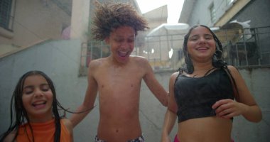 Çocuklar arka bahçedeki eğlence sırasında su spreyinde gülüp oynuyorlar. Canlı bir açık hava ortamında arkadaşlarıyla enerjik ve tasasız anların tadını çıkarıyorlar.