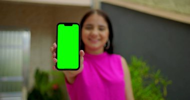 Genç kız gülümsüyor ve elinde yeşil ekranlı akıllı telefon ve kameraya yakın krom anahtar var. Dijital reklam için kişiselleştirilebilir ekranı vurguluyor.