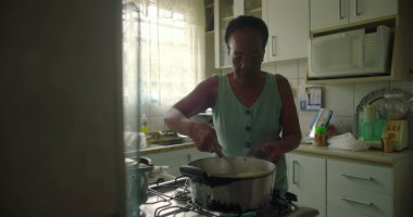 Afro-Amerikalı yaşlı bir kadın tencerede pirinç karıştırıyor. Yetenek, gelenek ve özel bir mutfak ortamında ev yapımı yemek hazırlama aşkı sergiliyor.