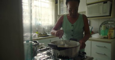 Afro-Amerikalı yaşlı bir kadın tencerede pirinç karıştırıyor. Yetenek, gelenek ve özel bir mutfak ortamında ev yapımı yemek hazırlama aşkı sergiliyor.