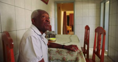 Sessiz bir mutfakta tek başına yemek masasında oturan yaşlı Afrikalı Amerikalı adam, huzur dolu bir ev ortamında yalnızlığı ve içselliği yansıtıyor.