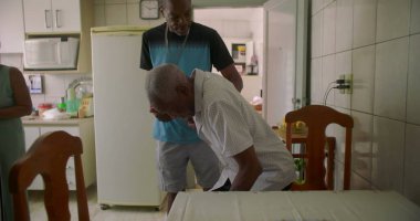 Oğlu tarafından desteklenen, koridorda yürüyen yaşlı Afrikalı Amerikalı bir adam, huzurlu bir ev ortamında bakım, yardım ve güçlü bir aile bağı sergiliyor.