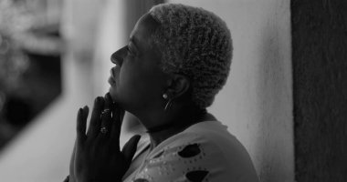 Afro-Amerikalı kadın duvara yaslanıyor, başını eğip dua ediyor, hayatın zorlukları arasında duygusal hassasiyetini ve güç umudunu ifade ediyor.