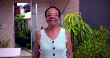 Yaşlı Afro-Amerikan kadın kendinden emin bir şekilde gülümsüyor. Çevresi yeşillik, aktif yaşam tarzı ve son yıllardaki pozitif enerji ile çevrili.