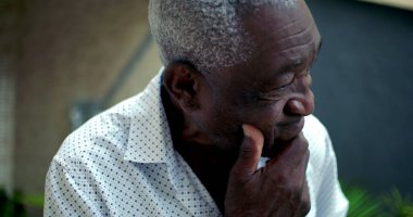 Yaşlı Afro-Amerikan bir adam, elinde dinleniyor, endişe ve pişmanlık gösteriyor, bir iç gözlem anında geçmiş kararları yansıtıyor açık hava ortamında