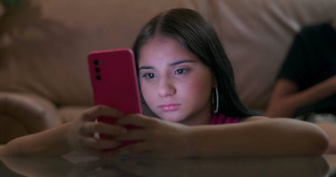 Akıllı telefona odaklanmış genç bir kız, sosyal medya bağımlılığı belirtileri, çevreden kopuk, teknoloji bağımlılığını vurgulayan, parlayan ışık