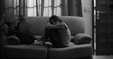 Kanepede oturan genç bir kız, bacakları vücuduna yakın tutulmuş, kafası kollarında dinleniyor, izolasyon, çocukluk bunalımı ve akıl hastalığı belirtileri gösteriyor.