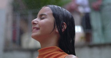 Genç kız ferahlatıcı su spreyini kucaklıyor, gülümsüyor ve arkasına yaslanıyor, mutluluğu yakalıyor, kaygısız anları yakalıyor, ve sıcak havada keyif alıyor.