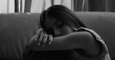 Kanepede oturan genç bir kız, bacakları vücuduna yakın tutulmuş, kafası kollarında dinleniyor, izolasyon, çocukluk bunalımı ve akıl hastalığı belirtileri gösteriyor.