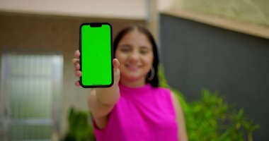 Genç kız gülümsüyor ve elinde yeşil ekranlı akıllı telefon ve kameraya yakın krom anahtar var. Dijital reklam için kişiselleştirilebilir ekranı vurguluyor.