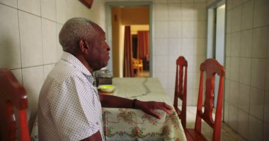 Sessiz bir mutfakta tek başına yemek masasında oturan yaşlı Afrikalı Amerikalı adam, huzur dolu bir ev ortamında yalnızlığı ve içselliği yansıtıyor.