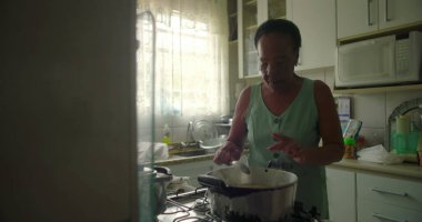 Afro-Amerikalı yaşlı bir kadın tencerede pirinç karıştırıyor. Yetenek, gelenek ve özel bir mutfak ortamında ev yapımı yemek hazırlama aşkı sergiliyor.
