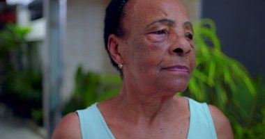 Yaşlı Afrikalı Amerikalı kadın düşünceli bir ifadeyle yan yana bakıyor, açık hava bahçe ortamında yan profil, son sınıflardaki yansıma ve huzur kavramı.