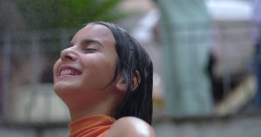 Genç kız ferahlatıcı su spreyini kucaklıyor, gülümsüyor ve arkasına yaslanıyor, mutluluğu yakalıyor, kaygısız anları yakalıyor, ve sıcak havada keyif alıyor.