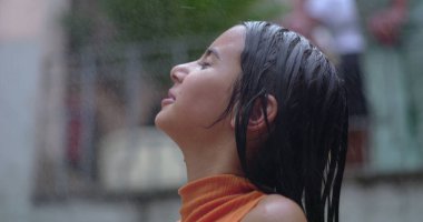 Genç kız ferahlatıcı su spreyini kucaklıyor, gülümsüyor ve arkasına yaslanıyor, mutluluğu yakalıyor, kaygısız anları yakalıyor, ve sıcak havada keyif alıyor.