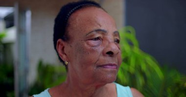 Yaşlı Afrikalı Amerikalı kadın düşünceli bir ifadeyle yan yana bakıyor, açık hava bahçe ortamında yan profil, son sınıflardaki yansıma ve huzur kavramı.