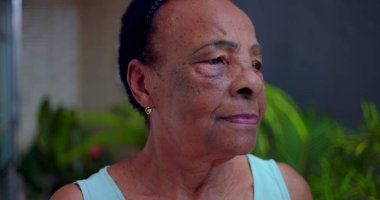Yaşlı Afrikalı Amerikalı kadın düşünceli bir ifadeyle yan yana bakıyor, açık hava bahçe ortamında yan profil, son sınıflardaki yansıma ve huzur kavramı.