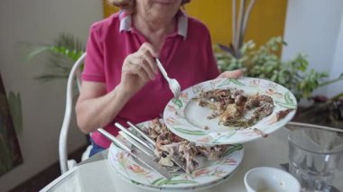 Yaşlı kadın, Yeşillik Balkon Masası 'ndaki Tavuk Kemikleri Yığını Elindeki Çatal ile Tabağı Temizliyor