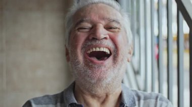 Yaşlı adam neşeli bir ifadeyle gülüyor. Açık ağızlı, kapının yanında duruyor.