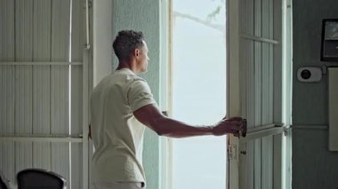 Bir adamın kapıyı açması ve Sunlit Caddesi 'ni karanlık garajdan gözlemesi şehir atmosferinin ortasında arama ya da beklenti olduğunu gösteriyor.