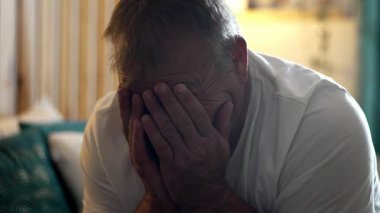 Yatakta oturan bir adam elleri ile yüzünü kapatıyor. Duygusal gerçekçilik ve yumuşak ışıkla samimi bir şekilde üzüntüsünü ve kırılganlığını gösteriyor.